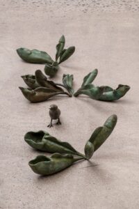 Three leaf sculptures surrounding a small figure of a bird. 