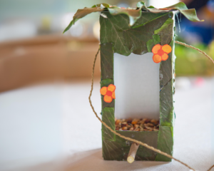 A milk carton filled with bird seed and covered in green leaves and orange flowers.
