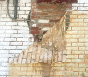 a sheet of latex is peeling from the brick surface of a building