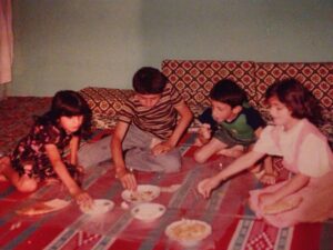 Four children sitting on a bright patterned rug on the floor eating with their hands.