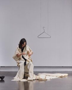 A woman sitting in a gallery with fabric around her, stitching into it.