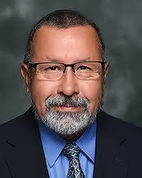 Dean Jacobs is photographed in a dark suit wearing a blue shirt and multicoloured blue tie.